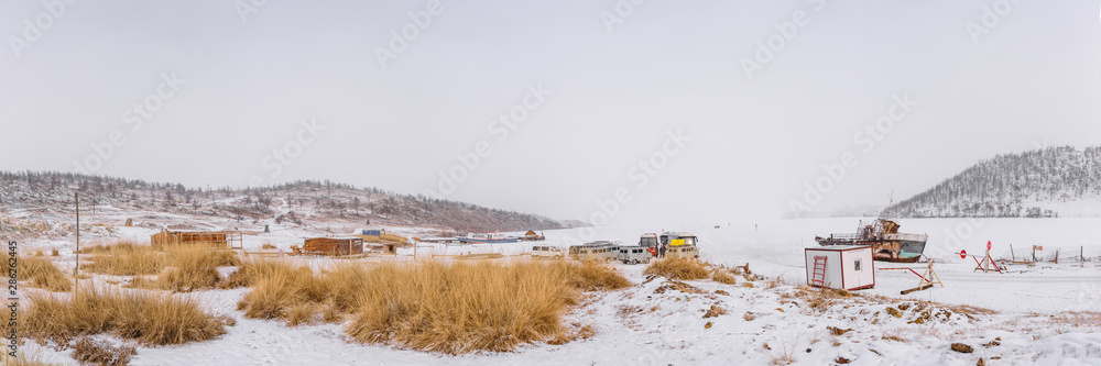 Icy ferry across frozen Lake Baikal to Olkhon Island, past a ship frozen in ice, on a snowy day with the sun covered by clouds.