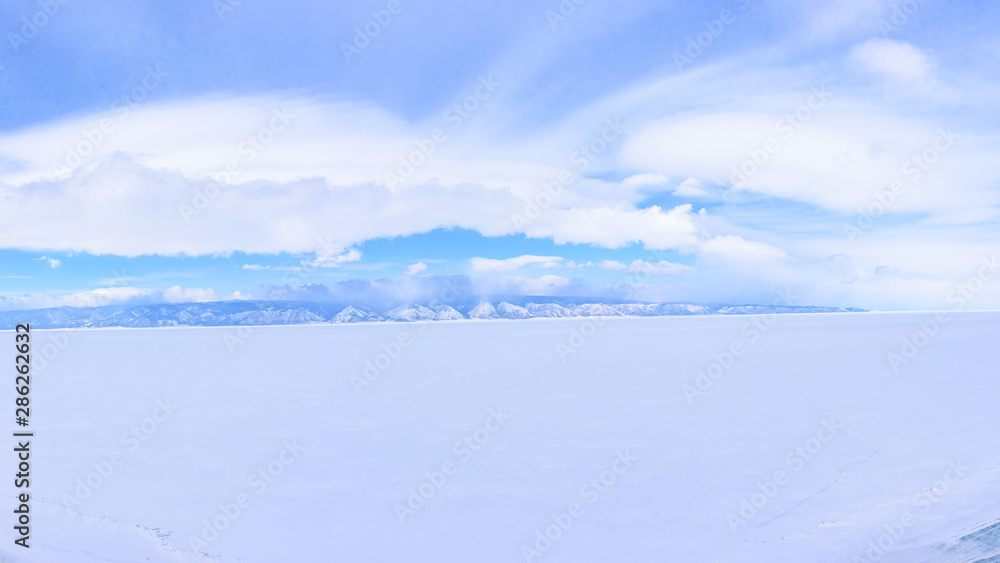 Snow-covered Lake Baikal with clouds in the sky with a view of the mountain on the opposite bank. 180 degree panorama.