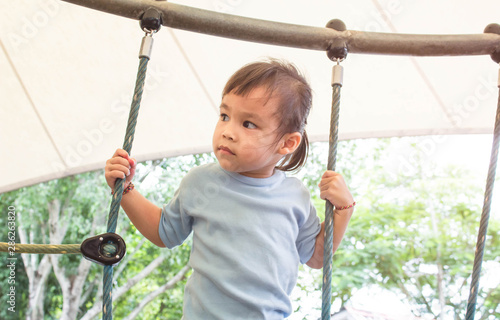 Asian little child girl having fun to climbing rope at playground in summer time.