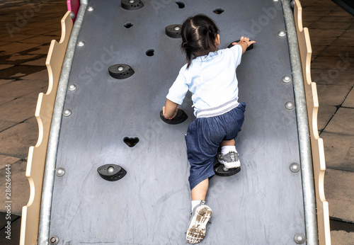 Rear of Asian little child girl climbing to slide at playground.