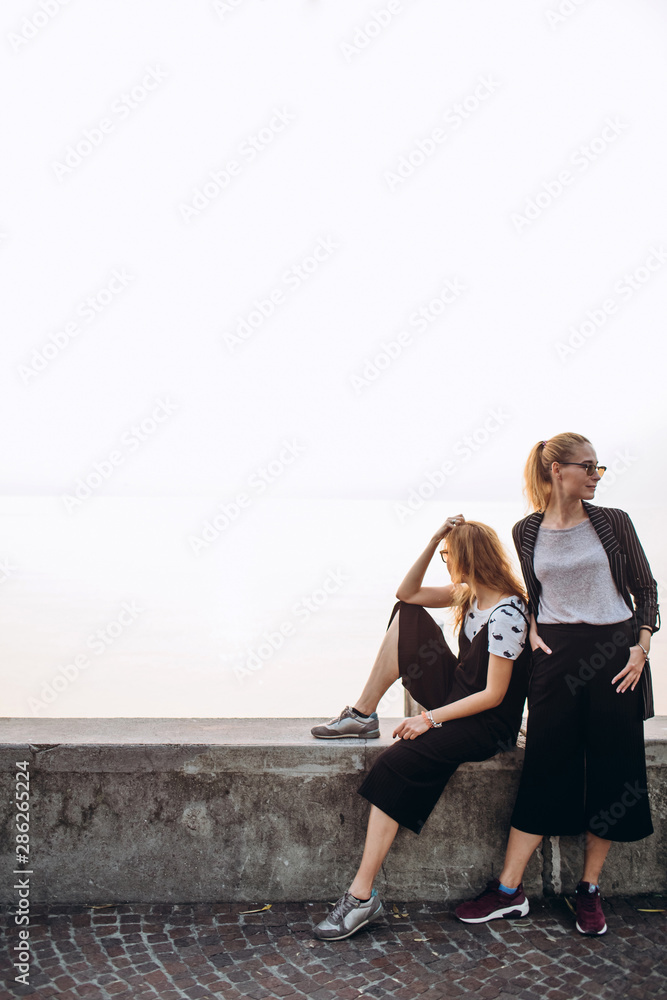 Girls are walking along the promenade on Lake Garda, Italy. Blonde girls in sunglasses are walking on the pier against the background of the lake.