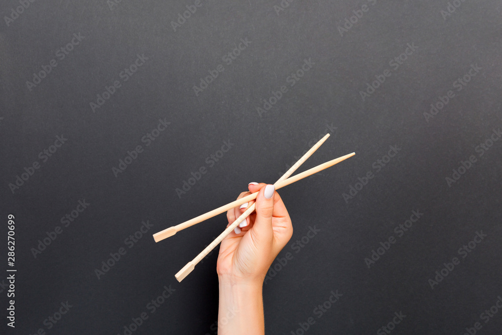 Fototapeta premium Female hand holding chopsticks on black background. Sushi concept with empty space for your idea