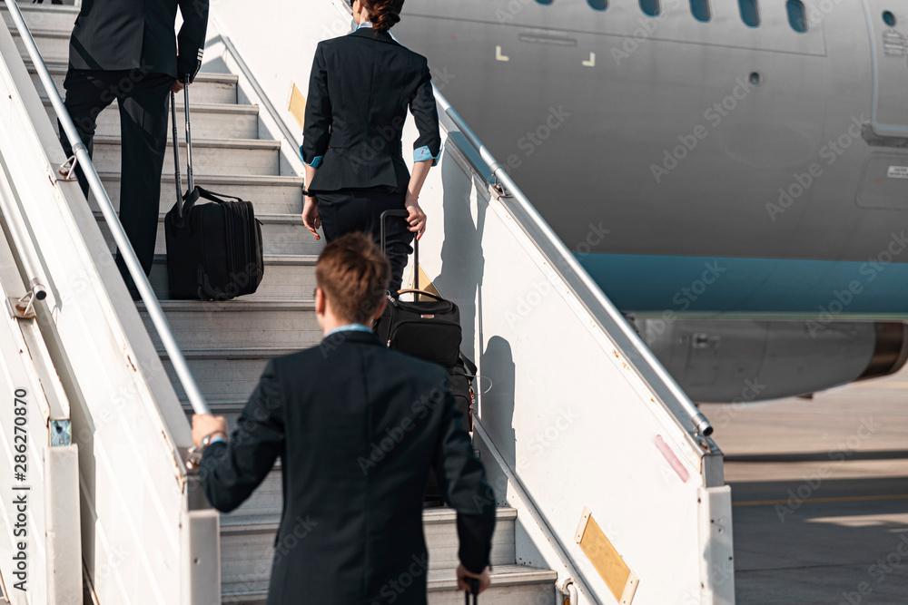 Adult Caucasian pilots and flight attendant going up on plane ladder Adult Caucasian pilots and flight attendant going up on plane ladder