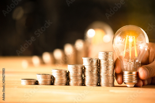 Hand holding a light bulb with coins stack. Creative ideas for saving money concept. Money management for the future