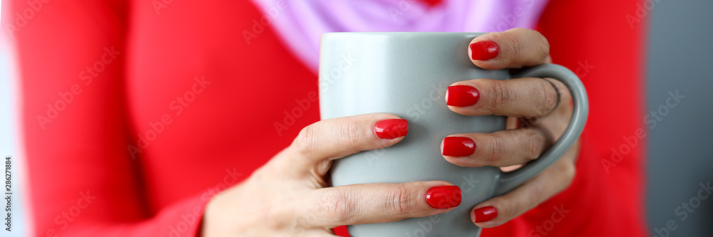 Female hands with red nails holding gray cup of coffee Female hands with red nails holding gray cup of coffee
