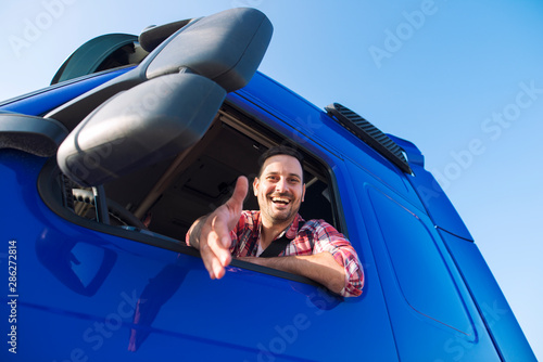 Truck drivers job openings. Truck driving careers. Middle aged professional trucker driver sitting in his vehicle cabin and giving shaking to new recruits. Drivers wanted. photo