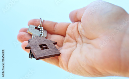 The mental key from door with wooden trinket in shape of house in woman's hand in front of sky