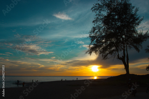 Silhouette of people and big tree on beach background with sunrise and blue sky.