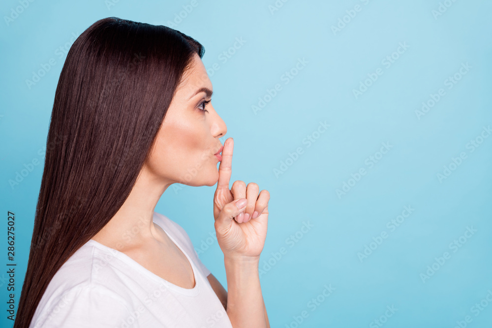 Close up copyspace photo of charming cute woman showing point finger on her lips for all to keep silent while isolated with blue background Close up copyspace photo of charming cute woman showing point finger on her lips for all to keep silent while isolated with blue background