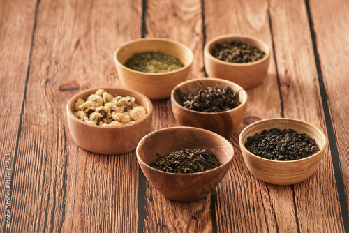 assortment of dry tea in white bowls on wooden surface