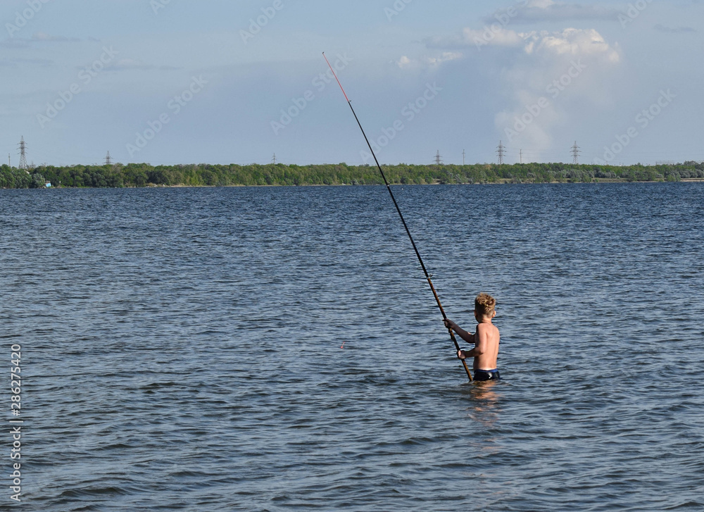 Young boy with a home fishing rod. Fishing in the lake on a summer day. Little fisherman is fishing. Boy learns to fish. Young boy with a home fishing rod. Fishing in the lake on a summer day. Little fisherman is fishing. Boy learns to fish.