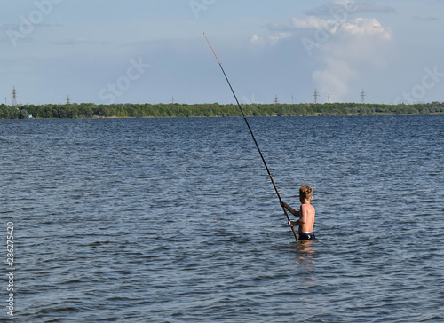 Young boy with a home fishing rod. Fishing in the lake on a summer day. Little fisherman is fishing. Boy learns to fish.