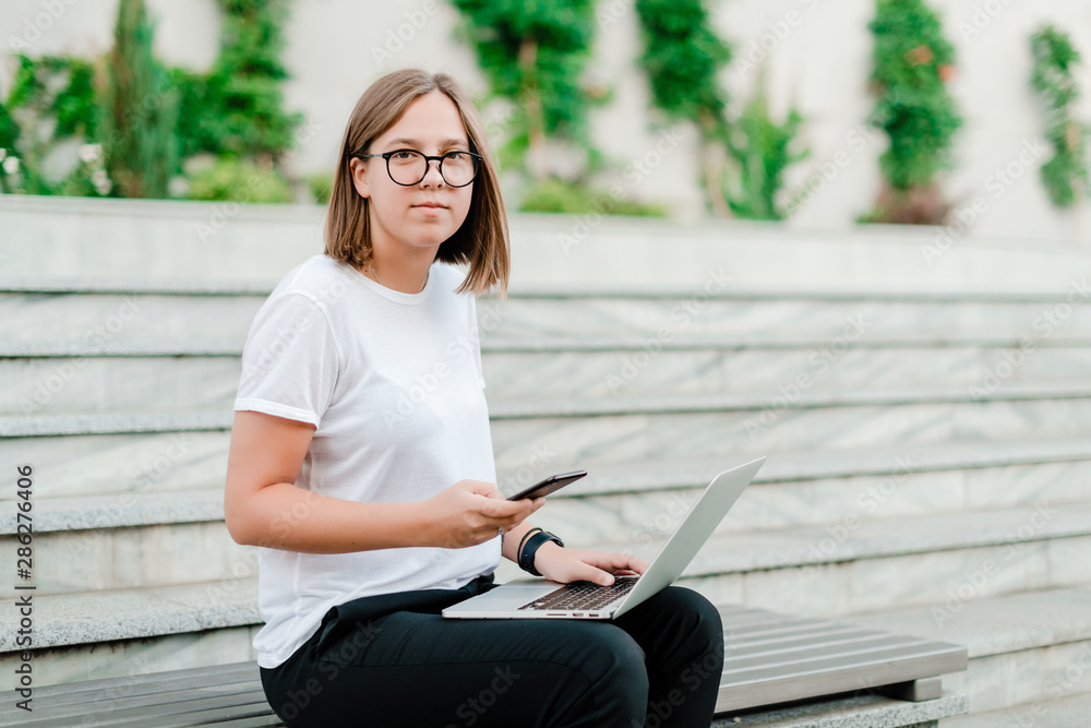 woman using phone and laptop for freelance work outdoors