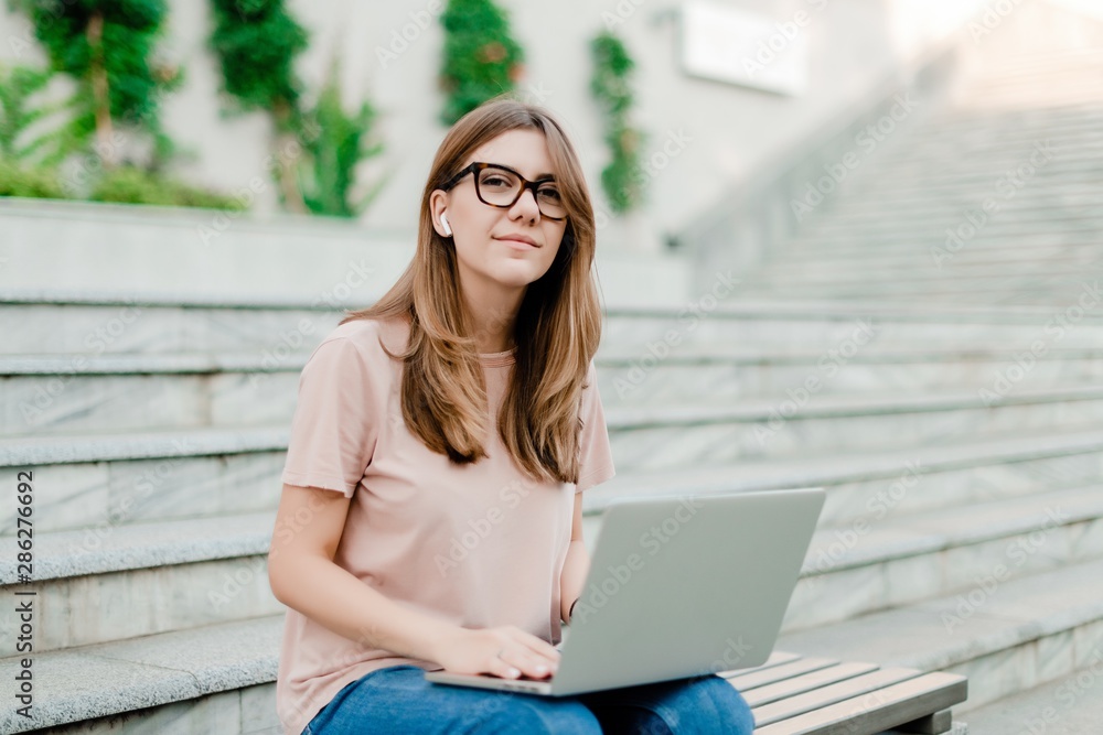 young woman with laptop smiling and working remotely outdoors young woman with laptop smiling and working remotely outdoors
