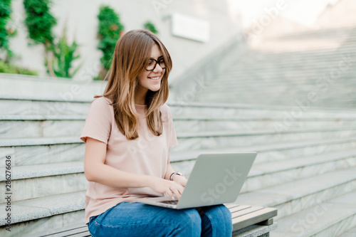 young woman freelancer using laptop and smiling outdoors