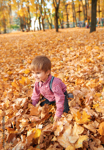 Happy child playing  posing  smiling and having fun in autumn city park. Bright yellow trees and leaves