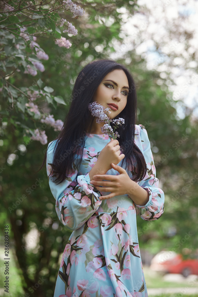 Brunette woman in the branches of a beautiful flowering tree. Short summer dress on the girl body. Spring walk in the Park, romantic mood. Portrait of a girl near bushes and trees Brunette woman in the branches of a beautiful flowering tree. Short summer dress on the girl body. Spring walk in the Park, romantic mood. Portrait of a girl near bushes and trees