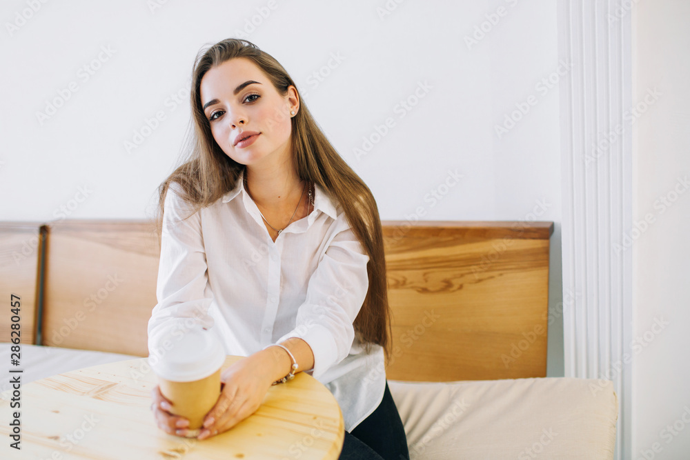 Attractive young woman with long hair is sitting at the table in a cafe with a cup of coffee. Attractive young woman with long hair is sitting at the table in a cafe with a cup of coffee.