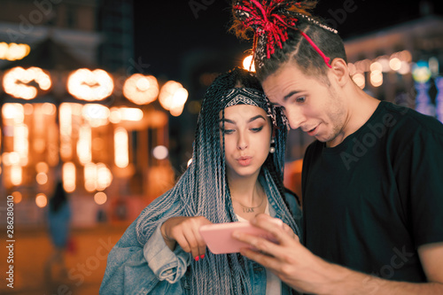 Young caucasian couple looking down at smartphone app in night city