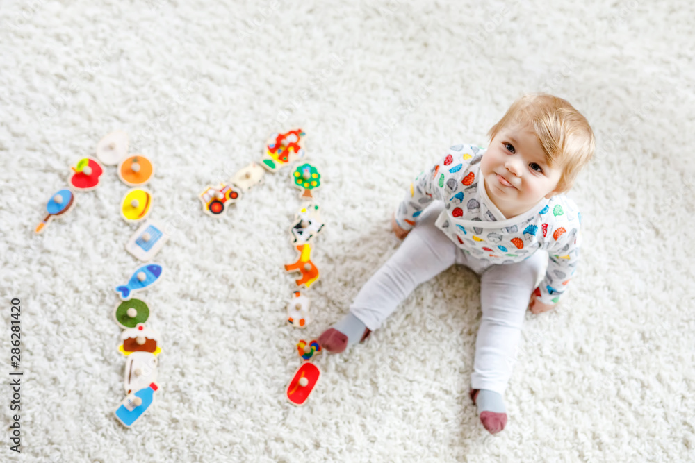 Naklejka premium Gorgeous cute beautiful little baby girl playing with educational toys like wooden puzzle at home or nursery. Happy healthy child having fun with colorful different toys. Kid learning different skills