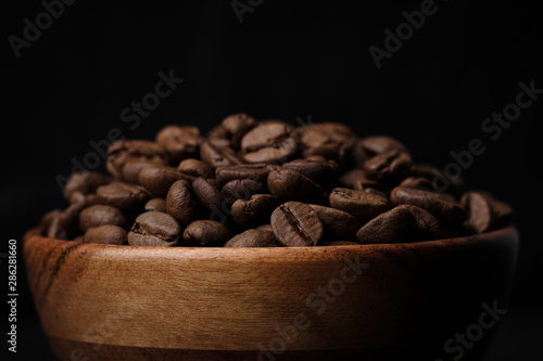 roasted coffee beans in wood bowl on black background. close up