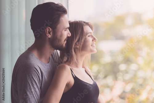 Couple hugging together. White youngman and woman standing near window with autum leafs in background. Happy smile together. With light leaks. photo