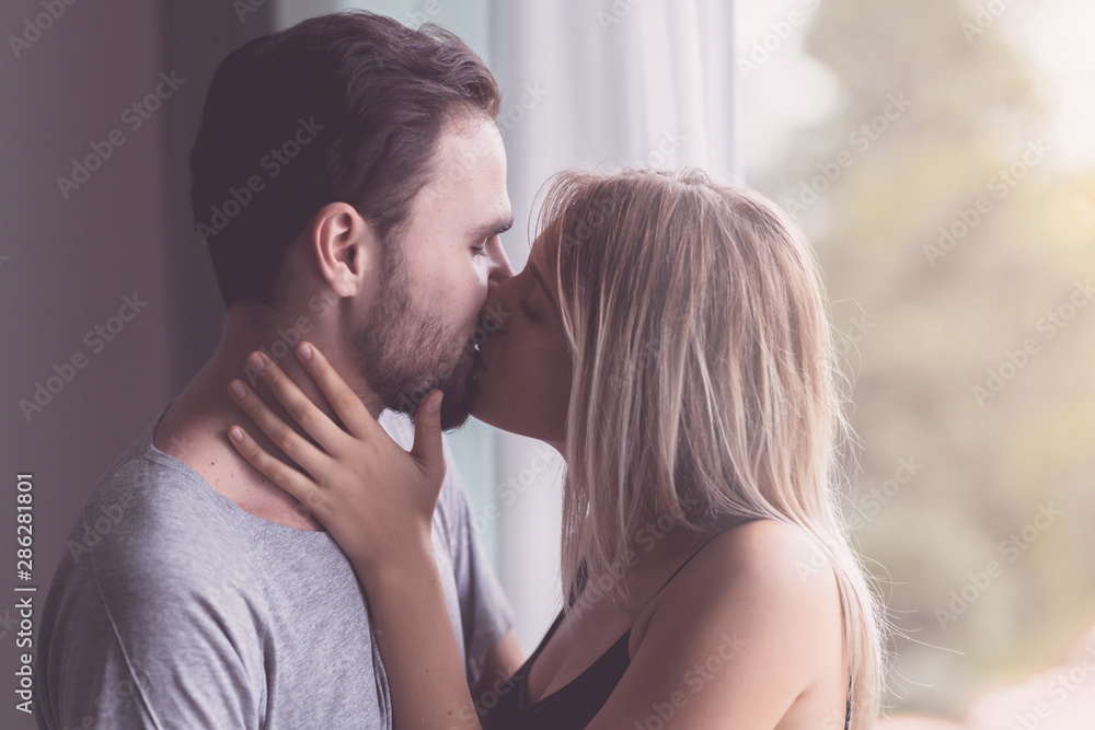 Couple hugging together. White youngman and woman standing near window with autum leafs in background. Holding and kissing her husband. With light leaks. Couple hugging together. White youngman and woman standing near window with autum leafs in background. Holding and kissing her husband. With light leaks.