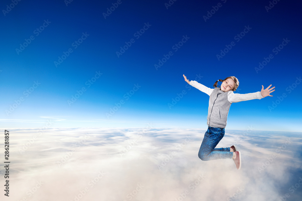 Little girl flying over clouds in the blue sky.