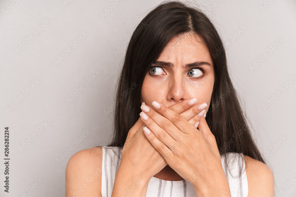 Image closeup of terrified woman with long dark hair covering her mouth with fear Image closeup of terrified woman with long dark hair covering her mouth with fear