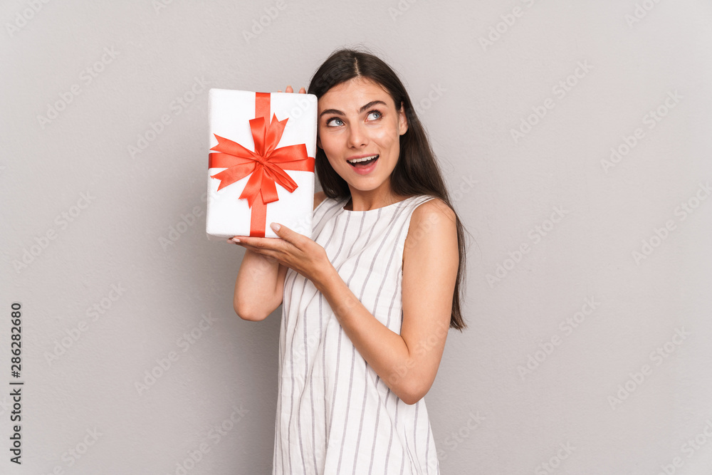 Image of excited brunette woman wearing dress smiling and holding present box Image of excited brunette woman wearing dress smiling and holding present box