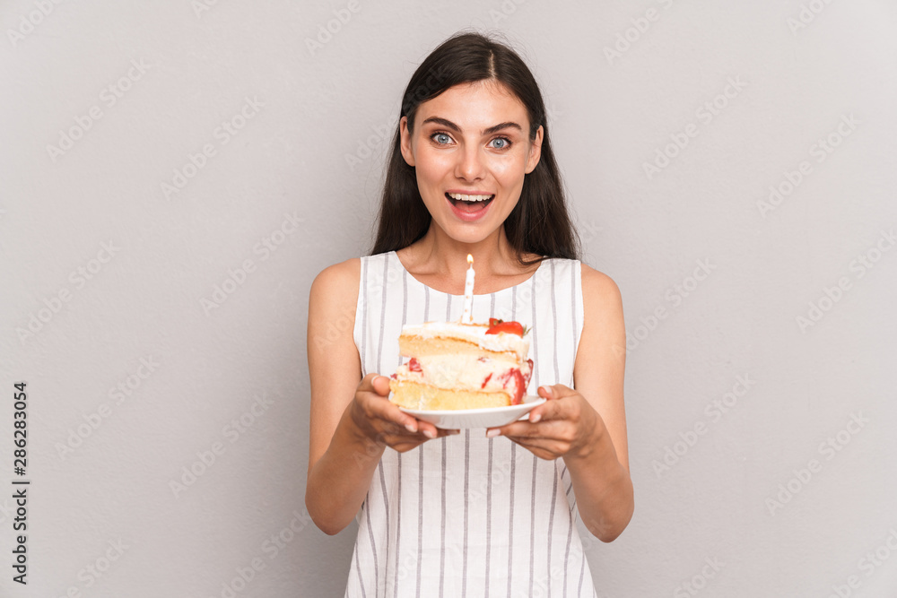 Image of beautiful brunette woman wearing dress smiling and holding birthday cake with candle Image of beautiful brunette woman wearing dress smiling and holding birthday cake with candle