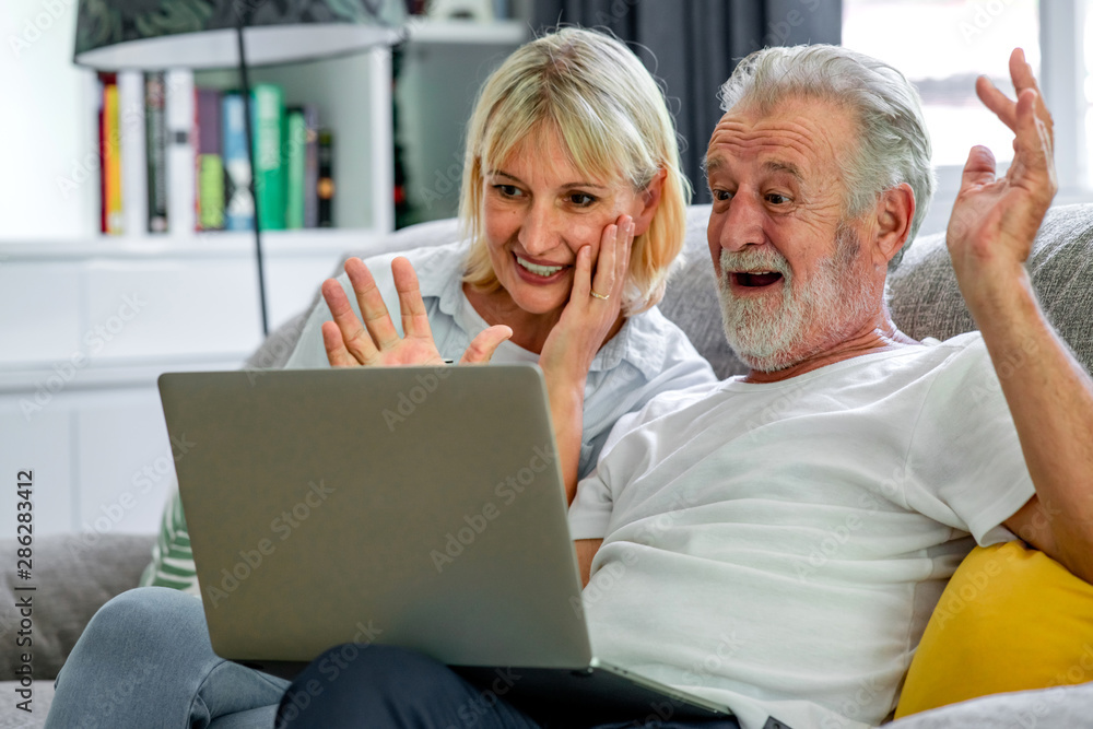 Senior couple using laptop in living room. White man and woman sitting on couch looking at laptop. Surprise mood.