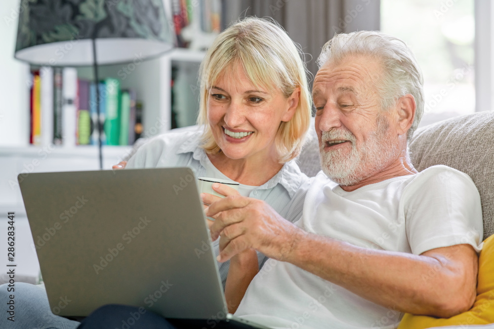 Senior couple using laptop in living room. White man and woman sitting on couch looking at laptop. Enjoy watching movie together. Senior couple using laptop in living room. White man and woman sitting on couch looking at laptop. Enjoy watching movie together.