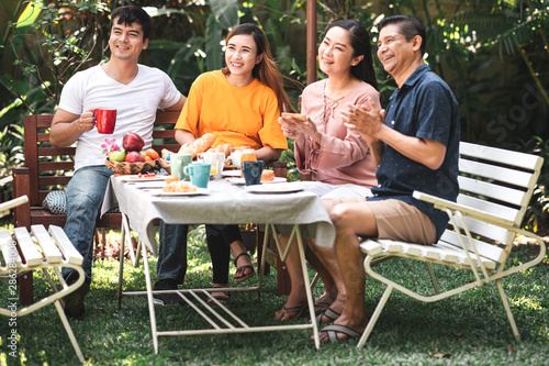 Family lunch outdoor. Married mix race couple with grand parents. White man, Asian pregnant woman with senior asian couple in tropical garden. Enjoying conversation together.
