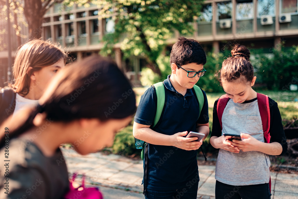 Obraz premium Classmates using smart phone at schoolyard
