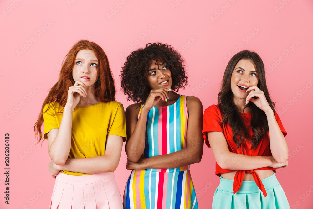 © Drobot Dean - Thinking young three multiethnic girls friends posing isolated over pink wall background looking aside.