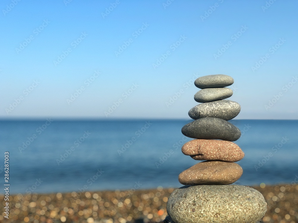 Marine theme: stones on the shore. The stones are stacked in a pyramid against the background of the sea. Pyramid of small stones on the beach. The concept of harmony of balance and meditation. Marine theme: stones on the shore. The stones are stacked in a pyramid against the background of the sea. Pyramid of small stones on the beach. The concept of harmony of balance and meditation.