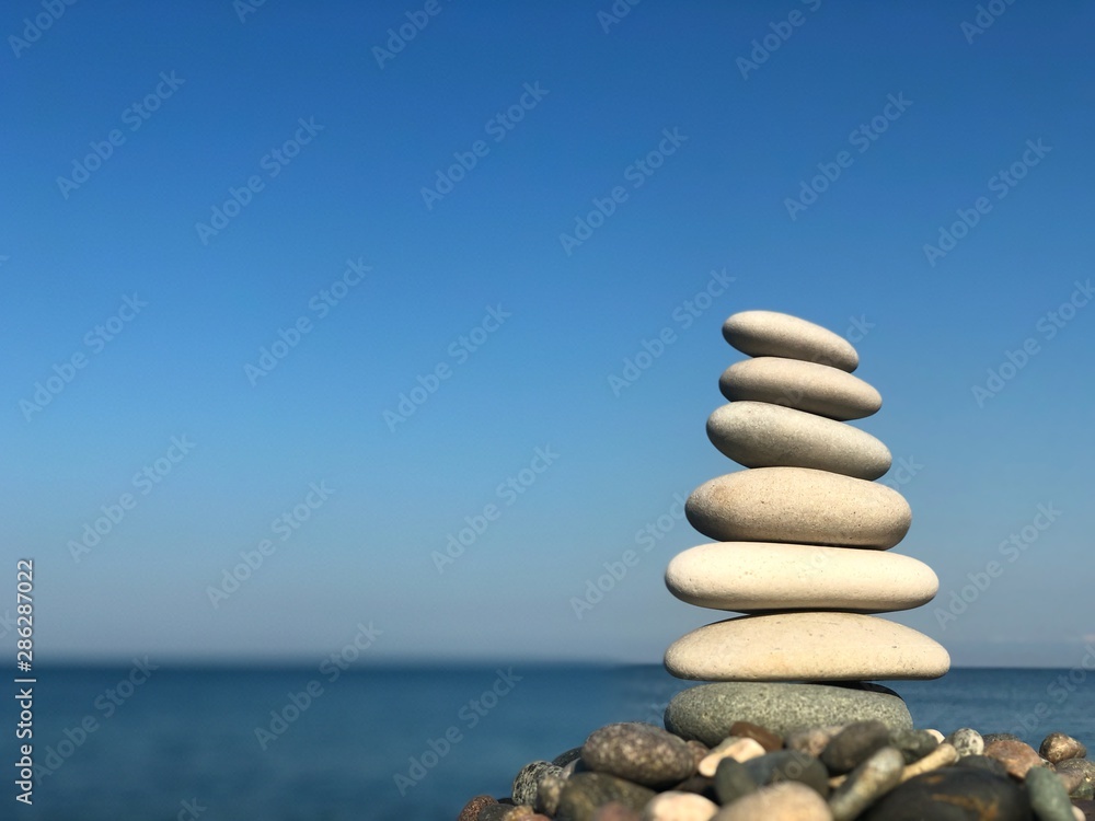 Fototapeta premium Marine theme: stones on the shore. The stones are stacked in a pyramid against the background of the sea. Pyramid of small stones on the beach. The concept of harmony of balance and meditation. 
