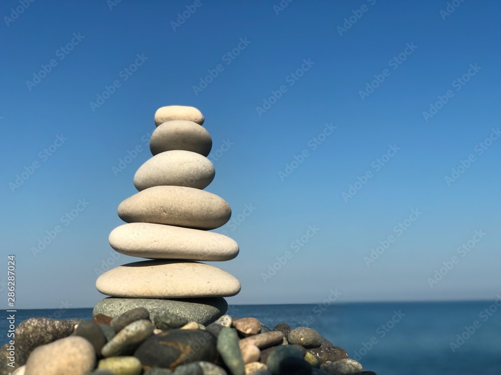 Marine theme: stones on the shore. The stones are stacked in a pyramid against the background of the sea. Pyramid of small stones on the beach. The concept of harmony of balance and meditation. Marine theme: stones on the shore. The stones are stacked in a pyramid against the background of the sea. Pyramid of small stones on the beach. The concept of harmony of balance and meditation.