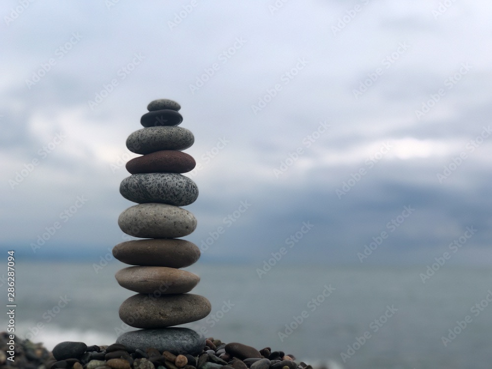 Marine theme: stones on the shore. The stones are stacked in a pyramid against the background of the sea. Pyramid of small stones on the beach. The concept of harmony of balance and meditation. Marine theme: stones on the shore. The stones are stacked in a pyramid against the background of the sea. Pyramid of small stones on the beach. The concept of harmony of balance and meditation.
