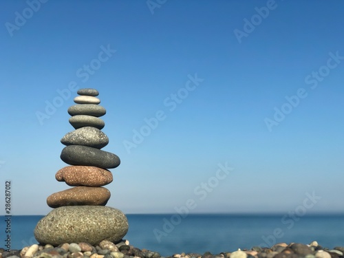 Marine theme: stones on the shore. The stones are stacked in a pyramid against the background of the sea. Pyramid of small stones on the beach. The concept of harmony of balance and meditation. 