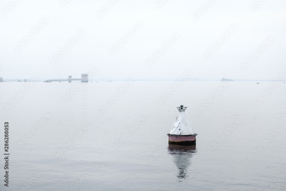 white buoy on the water in the fog. white on white