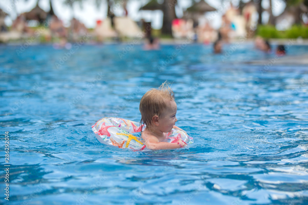 Adorable happy little child, toddler boy, having fun relaxing and playing in a pool in inflatable ring on sunny day during summer vacation