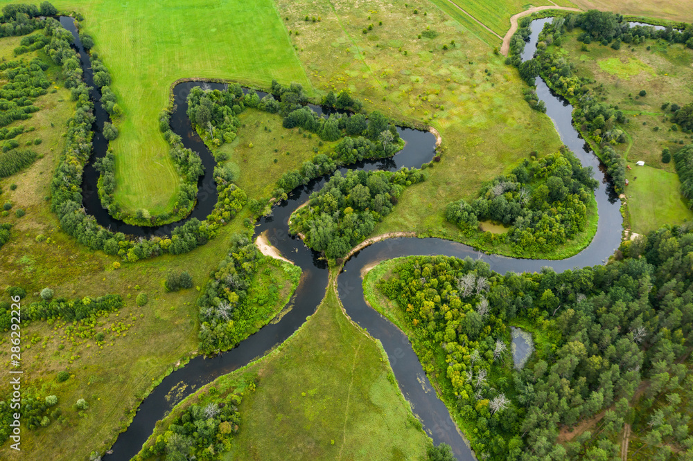 Top view drone shot of a green field, forest and river