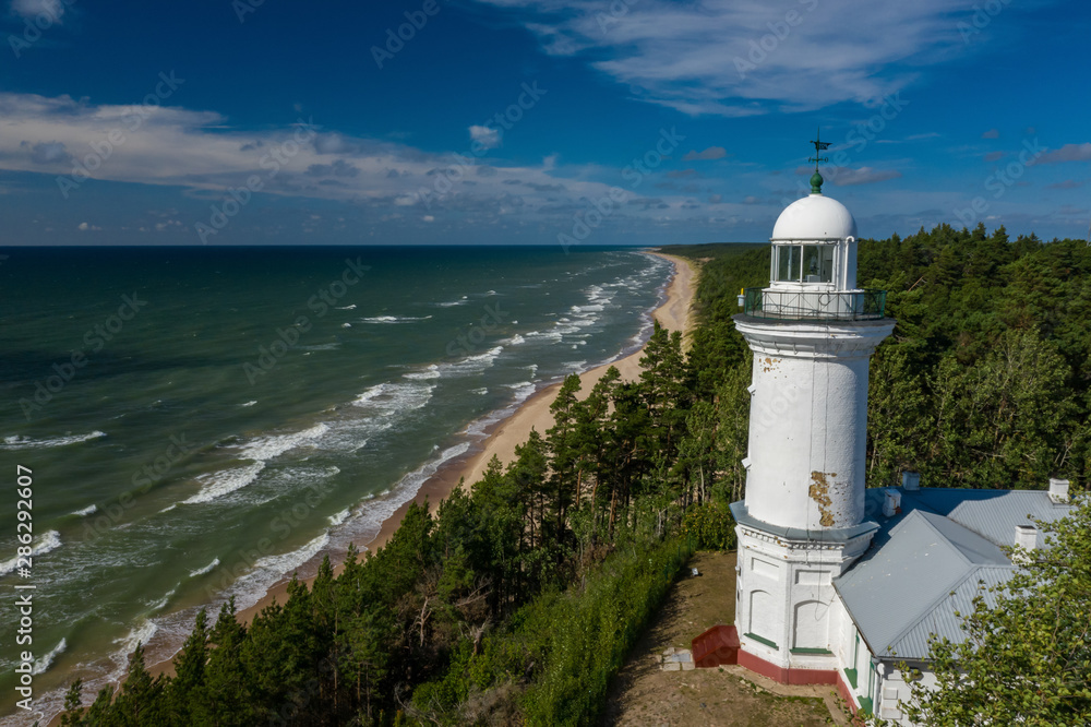 Top view of the sea and the Uzhava lighthouse. Blue sky. Green forest.