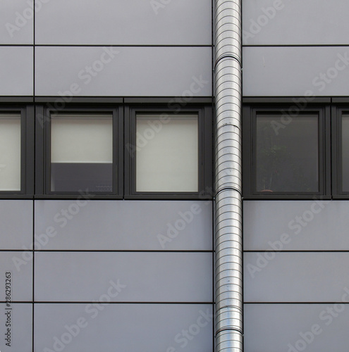 grey cladding panels on an industrial building with a row of back window frames and a silver pipe running up the wall photo