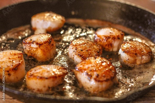 Selective Focus closeup of perfectly seared fresh sea scallops in butter and cracked pepper, sizzling on a cast iron skillet