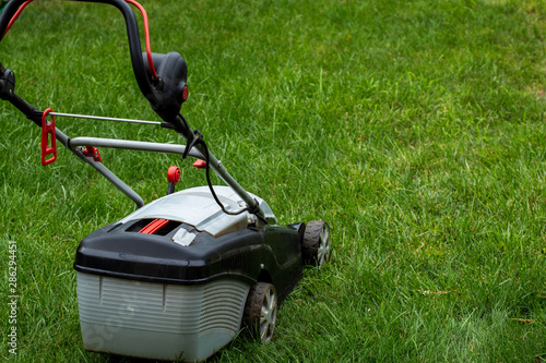 The gardener mows the grass with electric mower. Work in the garden, spring cleaning. Care for the garden and grass