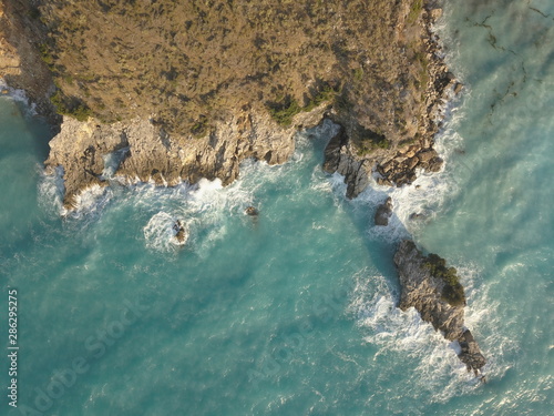 Aerial view of small beach with turquoise water next to rocks and trees in the area of Agia Paraskevi Halkidiki, Greece. View from drone