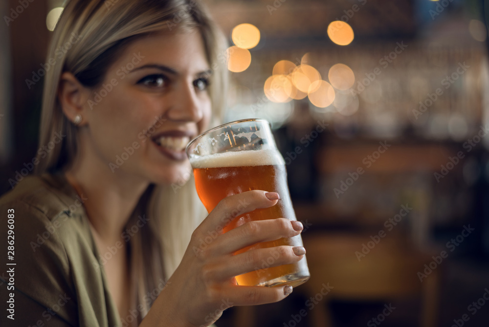 Close up of happy woman with glass of beer in a pub and looking away